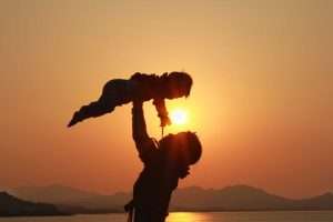 Parent lifting child at sunset silhouette.