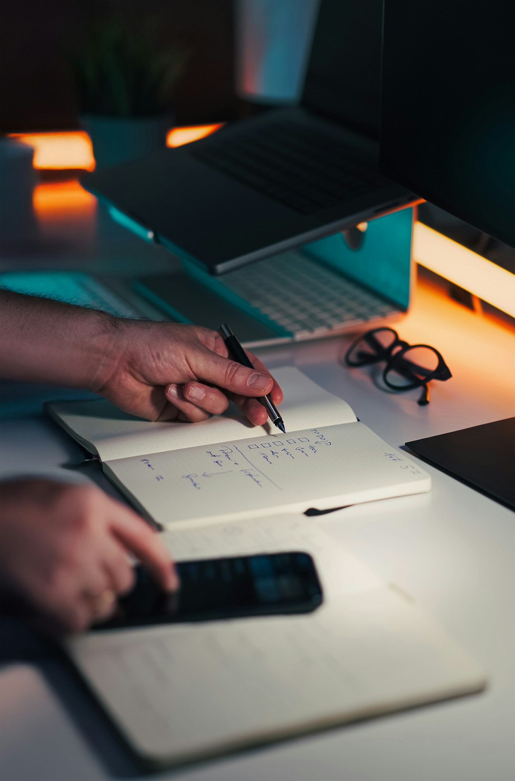 Hands writing a checklist near a laptop and phone, representing executive-function planning.
