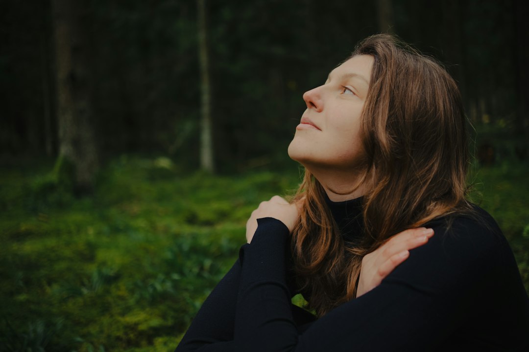 Person with eyes closed in a forest representing a calming pause and self-compassion